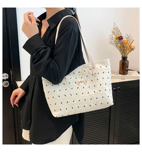 Detail of white tote bag featuring black bow patterns and a golden bow metal buckle