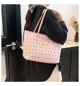 Detail of pink tote bag with floral embossing, gold bow hardware, and shoulder straps