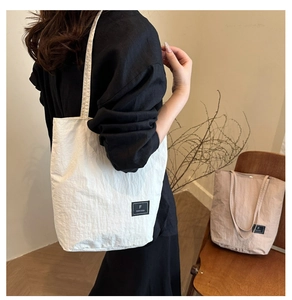 Detailed view of lightweight nylon tote bags in white and beige showing branding labels