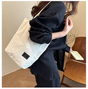 Detail of white canvas bucket bag featuring a black leather logo patch and natural texture