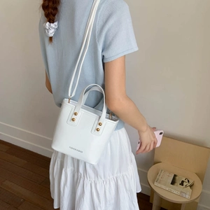 White leather bucket bag with gold rivets and shoulder strap worn by a female model