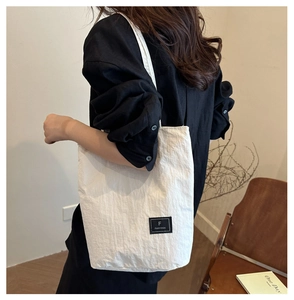 Detailed view of white nylon crossbody bag with black logo patch worn by a model