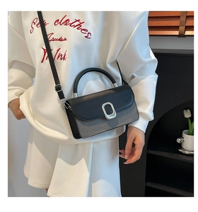 Close-up of stylish contrast-color crossbody bag with metallic buckle on white hoodie