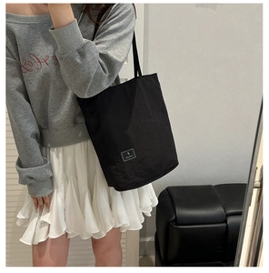 Shoulder view of a black nylon crossbody bag with white brand label and textured fabric