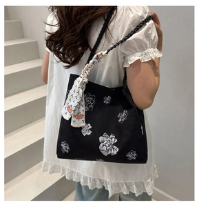 Detail of floral canvas tote bag with woven rope handle and decorative silk scarf accessory