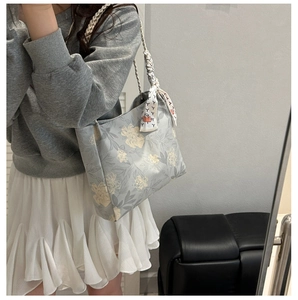 Detail of light blue floral shoulder bag with woven strap and decorative silk scarf
