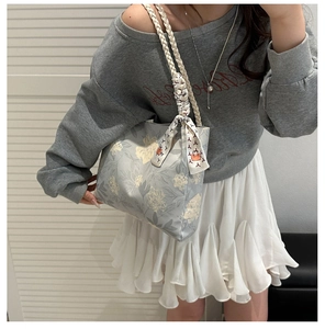 Détail du sac seau en toile fleurie avec poignée tressée et foulard sur un mannequin