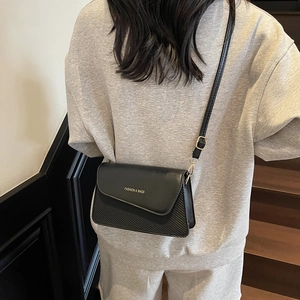 Minimalist black flap crossbody bag with carbon fiber texture and golden hardware accents
