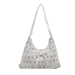 White hobo bag with black bow patterns, pleated texture, and heart pendant detail