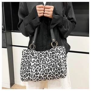Dettaglio borsa tote in tela leopardata con tracolla in pelle nera e anelli dorati