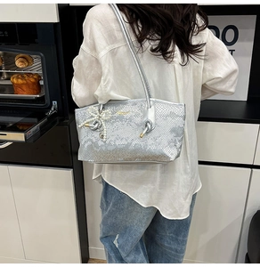 Silver snakeskin underarm bag with pearl bow charm worn by model in casual setting