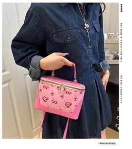 Detail view of a pink box bag with cherry print and golden metal zipper hardware