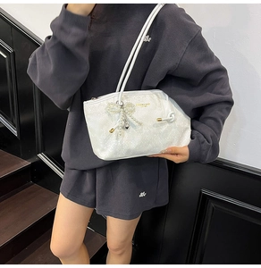 Detail of white faux snakeskin bag featuring pearl bow charm and golden lettering logo