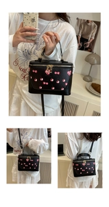 Detail of black box bag with cherry print, showing top handle and adjustable strap