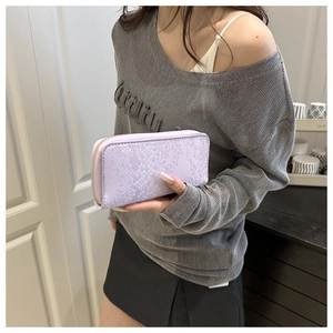 Close-up of lavender snakeskin patterned long wallet held by a model in casual setting