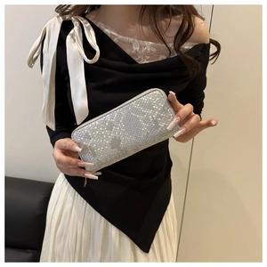 Close-up of silver snakeskin textured long wallet held by a model in a modern indoor setting