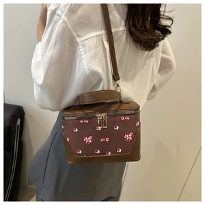 Detailed view of cherry print on a brown leather box bag carried by a model