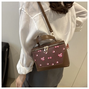 Detailed view of brown cherry print vanity bag with adjustable strap and top handle