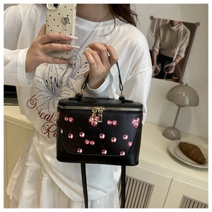 Detail of a black bucket bag featuring red cherry prints and golden metal zippers