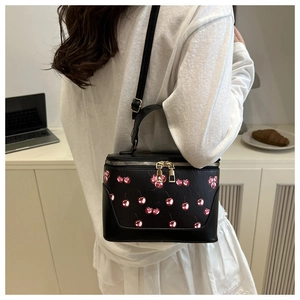 Detail of black box bag with cherry print and golden zipper shown in a lifestyle setting