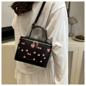 Detail of black matte crossbody bag with red cherry print and golden dual zippers