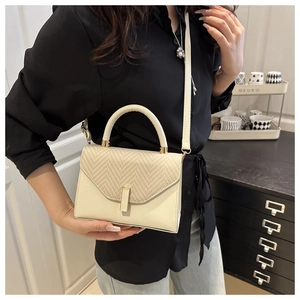 Detail view of cream white patchwork handbag with straw texture and gold buckle on a model