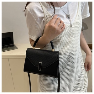 Detail of black lizard texture flap bag with gold hardware held by a model in casual chic outfit