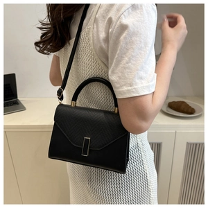 Detail of black trapezoid handbag with lizard skin texture and gold lock on model