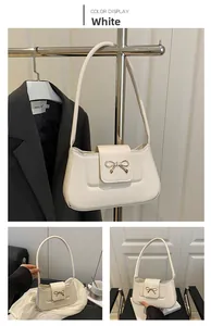 Close-up of white leather baguette bag with a golden metal bow buckle and shoulder strap