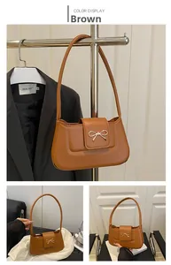 Detail of a brown shoulder bag featuring a gold metal bow and smooth synthetic leather