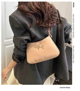 Chic beige shoulder bag with gold metal bow shown on model in grey blazer outfit