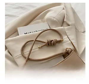 Detail of beige shoulder bag featuring rope knot strap and golden metal bow decoration