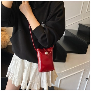 Detail of red glossy mini crossbody bag featuring a large pearl buckle closure