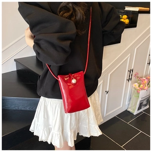 Detail of red glossy bucket bag featuring a white pearl clasp worn by a model