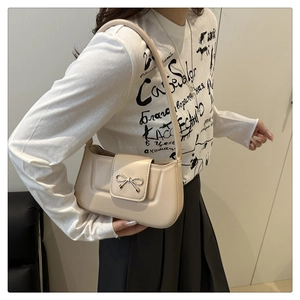 Détail d'un sac à bandoulière beige avec boucle nœud en métal porté par un mannequin