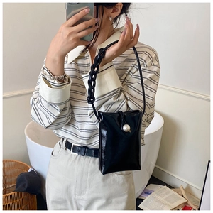 Detail of glossy black patent leather bag with a large pearl buckle and chunky chain