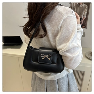 Detailed close-up of a black leather underarm bag featuring a gold bow buckle on the flap