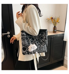 Detailed view of black graffiti canvas tote bag with white cloud plush pendant and long straps
