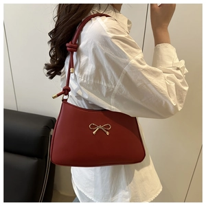 Close-up of a red leather underarm bag featuring a golden bow and knotted shoulder strap