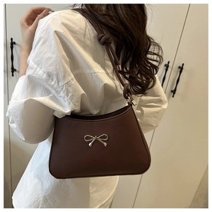 Detailed side view of deep coffee underarm bag with gold bow on minimalist wardrobe background