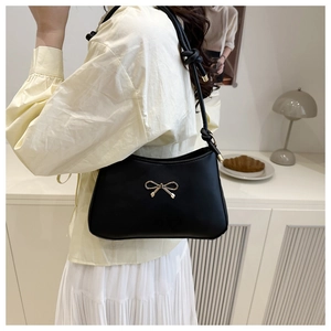 Detail of black leather shoulder bag featuring a gold bow ornament and knotted strap