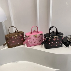 Three trendy cherry-printed box handbags in brown, pink and black on geometric pedestals