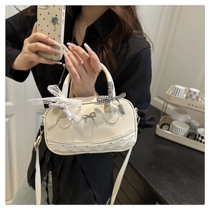 Detail of cream Boston bag with lace trim, bow charms and adjustable shoulder strap