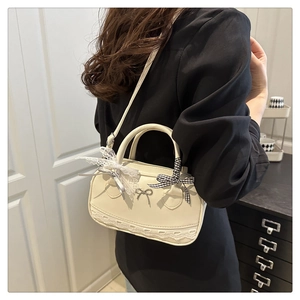 Detail of a creamy white handbag with lace trim, bows, and a slim shoulder strap