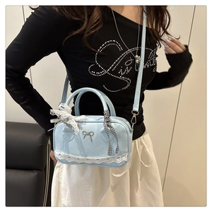 Close-up of light blue Boston bag with white lace trim and bow metal clasp detail