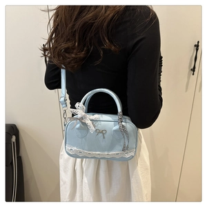 Detail of light blue crossbody bag with white lace trim and metal bow accent