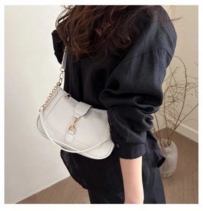 Detailed view of a white leather underarm bag with gold metal clasp on a black shirt