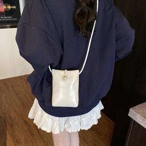 Mini sac carré crème à bandoulière avec boucle en perle porté par un mannequin chic