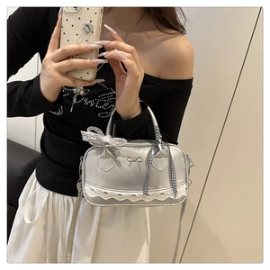 Detail of silver boston bag with lace trim, metallic bow, and checkered ribbon handle