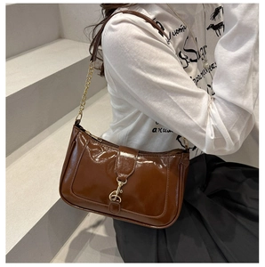 Gros plan du sac à bandoulière en cuir verni marron avec boucle dorée sur modèle